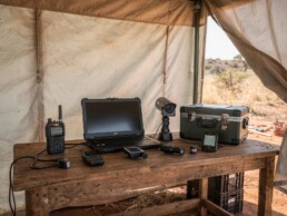 Field security workstation with rugged laptop, radios and surveillance devices for NGO media teams in remote environments.
